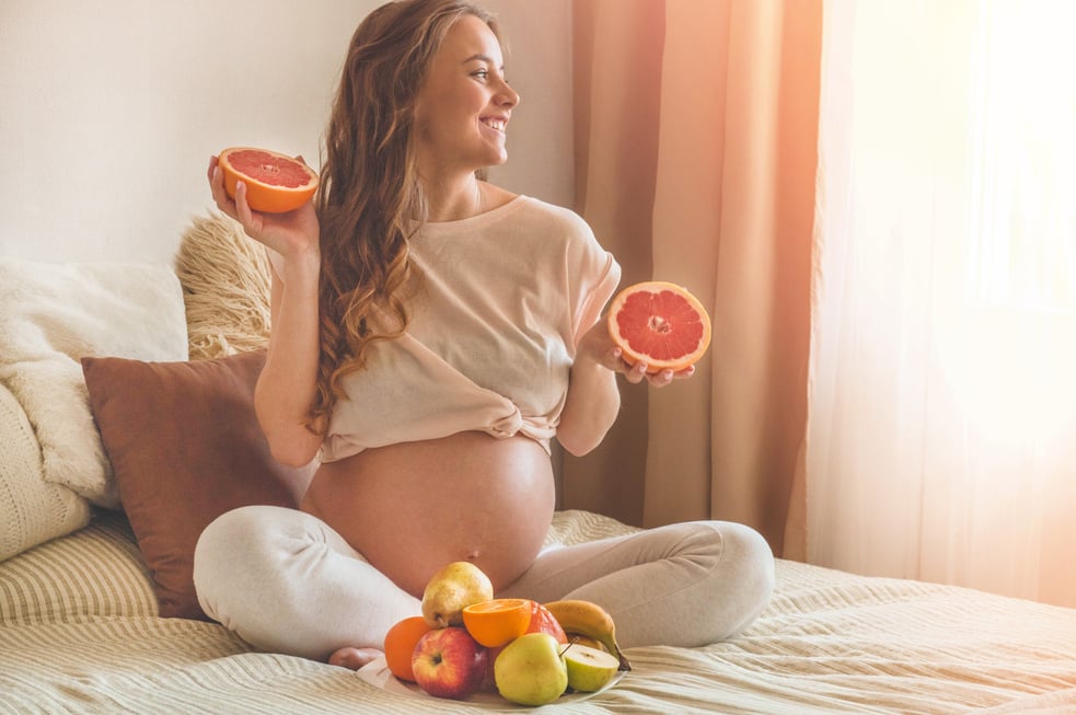 Pregnancy and healthy organic nutrition. Pregnancy and grapefruit. Pregnant woman enjoying fresh fruits in bed, free space. Concept of expectation and health.